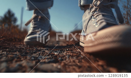 Low angle view of person's feet wearing sneakers on a textured, outdoor path. Low angle view of person's feet wearing sneakers on a textured, outdoor path. 128919135