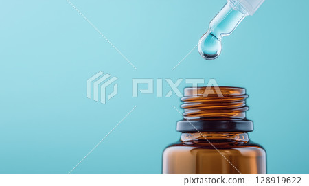 Dropper releasing droplet into amber glass bottle against blue background 128919622