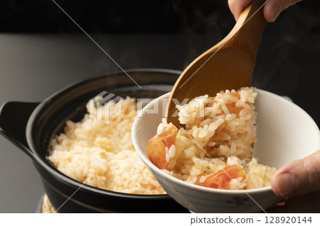 Steaming rice cooked in a clay pot with whole tomatoes is served in a rice bowl with a rice spoon. 128920144