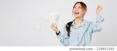 Excited Asian woman holding dollar money fan banknotes smiles with excitement, fist raised for success and money celebration. isolated studio white background 128921203
