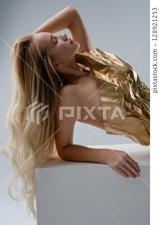 Beauty and elegance showcased in a studio with a blonde woman in a golden outfit Beauty and elegance showcased in a studio with a blonde woman in a golden outfit 128921253