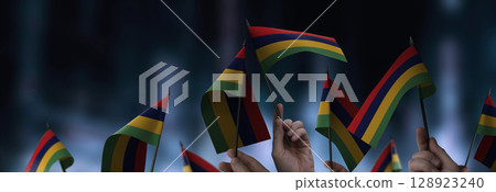 Mauritius flags in their hands on a blurred urban background 128923240