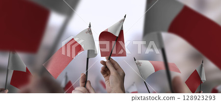 Malta flags in their hands on a blurred urban background 128923293