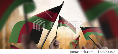 Malawi flags in their hands on a blurred urban background Malawi flags in their hands on a blurred urban background 128923302
