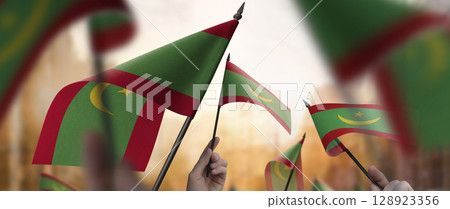 Mauritania flags in their hands on a blurred urban background Mauritania flags in their hands on a blurred urban background 128923356