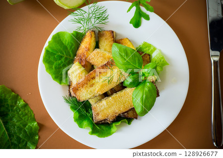 Fried zucchini slices with salad greens on a brown background Fried zucchini slices with salad greens on a brown background 128926677