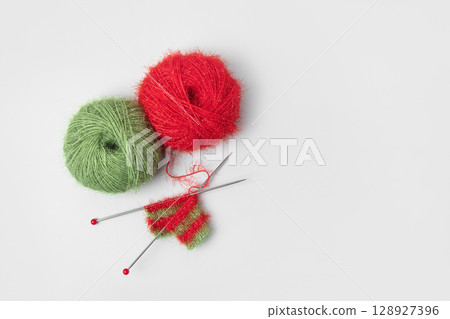 Red and green knitted wool on gray background with knitting needles for knitting warm clothes and hobbies needlework. Knitting a striped Christmas scarf with red and green threads Red and green knitted wool on gray background with knitting needles for knitting warm clothes and hobbies needlework. Knitting a striped Christmas scarf with red and green threads 128927396