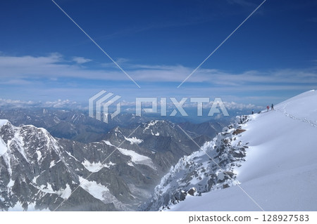 Adventurous hiker enjoying the breathtaking view from a snowy mountain peak 128927583