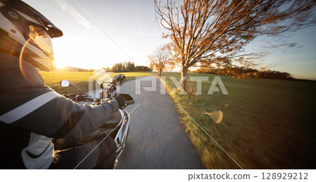 Driver riding motorcycle on empty road during sunset , view from the passenger side 128929212