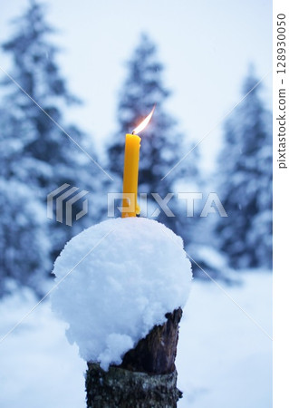 Candle is lit on top of a snow-covered log 128930050