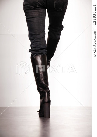 Woman wearing black boots and jeans is walking on a floor 128930111