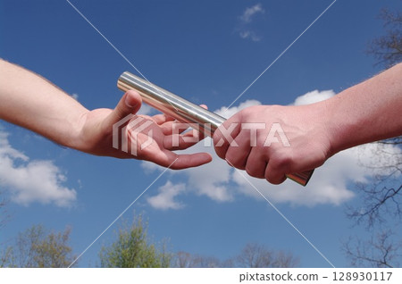 Two people are holding a baton and one is handing it to the other 128930117
