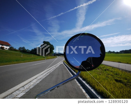 Mirror on a car is reflecting the sky and the road 128930120