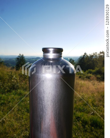 Silver water bottle is sitting on a grassy hillside Silver water bottle is sitting on a grassy hillside 128930129