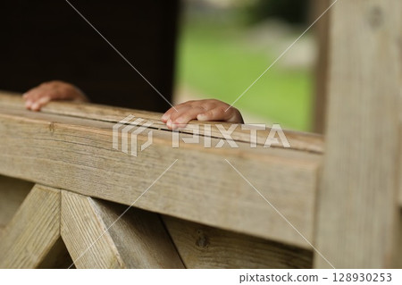 A wooden fence with two hands peeking out from behind it 128930253