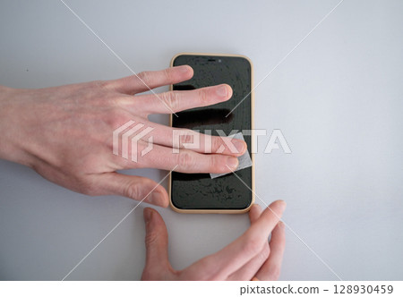 Man cleaning smartphone screen with dry wipe before applying screen protector 128930459