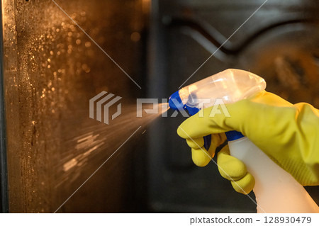 Person spraying degreaser inside dirty oven with yellow rubber gloves Person spraying degreaser inside dirty oven with yellow rubber gloves 128930479