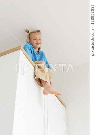 Joyful young girl climbing on a high cabinet having fun 128932053
