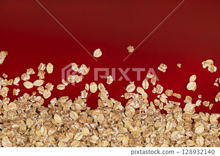 Close-up of raw rolled oats scattered on a bright red surface, creating a vibrant and healthy food concept. Close-up of raw rolled oats scattered on a bright red surface, creating a vibrant and healthy food concept. 128932140