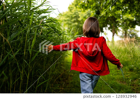 Young caucasian child walking in nature, red jacket, holding grass, outdoor adventure 128932946