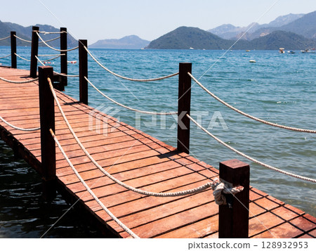Scenic wooden pier overlooking tranquil ocean with majestic mountains in background 128932953