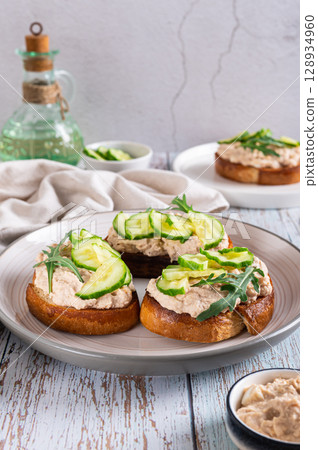 Appetizing sandwiches with cod liver pate, cucumber and arugula on a plate vertical view Appetizing sandwiches with cod liver pate, cucumber and arugula on a plate vertical view 128934960