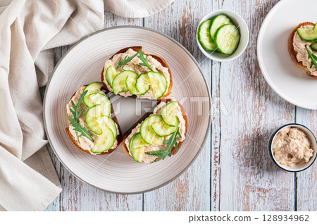 Appetizing sandwiches with cod liver pate, cucumber and arugula on a plate top view 128934962