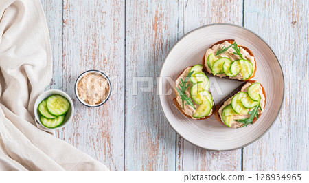 Homemade toasts with cod liver, cucumber and herbs on a plate on a table top view web banner Homemade toasts with cod liver, cucumber and herbs on a plate on a table top view web banner 128934965