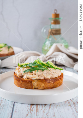 Cod liver, cucumber slices and arugula crostini on a plate on a table vertical view Cod liver, cucumber slices and arugula crostini on a plate on a table vertical view 128934968