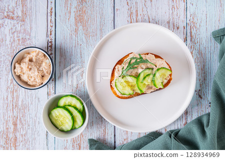 Cod liver, cucumber slices and arugula crostini on a plate on a table top view Cod liver, cucumber slices and arugula crostini on a plate on a table top view 128934969