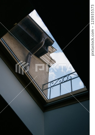 Skylight with sky view and balcony. The window offers a view of overcast sky with a few clouds. Skylight with sky view and balcony. The window offers a view of overcast sky with a few clouds. 128935573