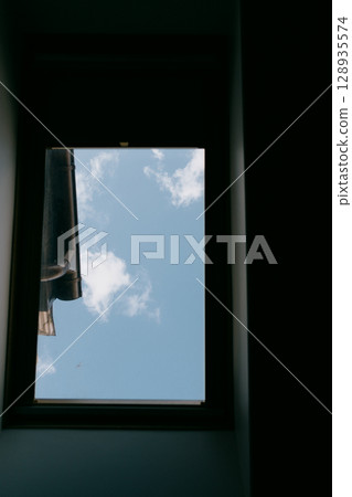 Skylight with sky view and balcony. The window offers a view of overcast sky with a few clouds.  128935574