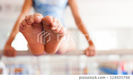 Bare tensed feet of female gymnast performing on parallel bars 128935798