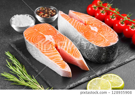 Two fresh raw salmon steaks with tomatoes, spices, rosemary and lime on black stone background 128935908