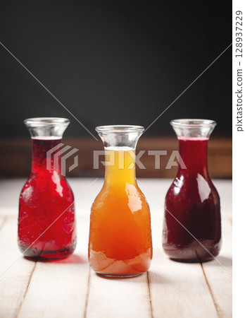 Glass carafes with red orange and purple juice 128937229