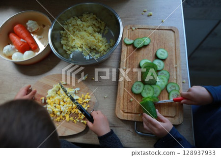 two child's hands cutting vegetables for salad close up two child's hands cutting vegetables for salad close up 128937933