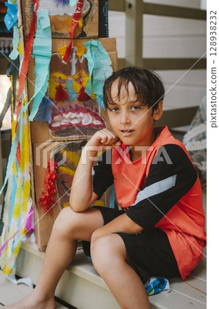 Creative Boy Sitting Beside Crafted Colorful Masks Creative Boy Sitting Beside Crafted Colorful Masks 128938232