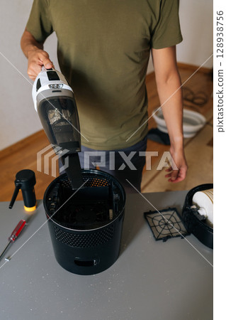 Vertical shot of cleaning company worker male cleaning air humidifier using handheld vacuum cleaner, performing thorough home device maintenance for optimal indoor air quality and cleanliness. 128938756