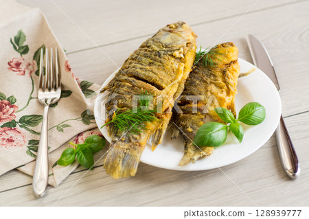 Fried crucian carp with a crispy golden crust on a white plate Fried crucian carp with a crispy golden crust on a white plate 128939777