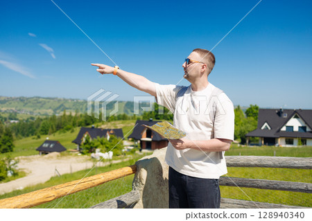 Smiling Man Pointing Ahead While Holding a Map in Mountain Village Smiling Man Pointing Ahead While Holding a Map in Mountain Village 128940340