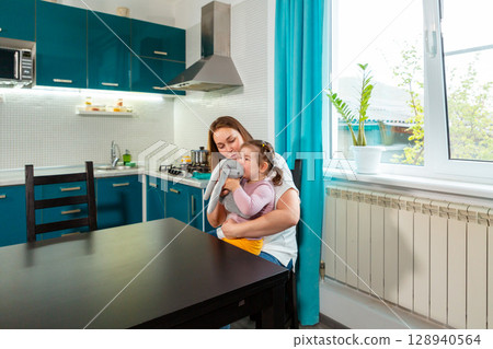 A mother or preschool educator helps a toddler express emotions and thoughts through structured playtime in a bright kitchen environment. A mother or preschool educator helps a toddler express emotions and thoughts through structured playtime in a bright kitchen environment. 128940564