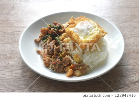 spicy stir fried slice beef meat with basil leaf and chili on rice topping egg in plate  128942416