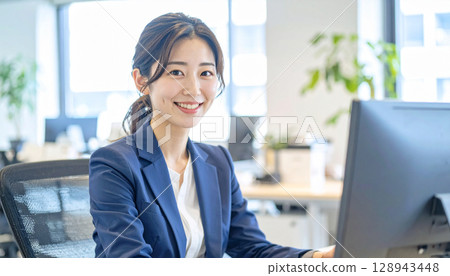 A young female office worker smiling and operating a PC in a clean office A young female office worker smiling and operating a PC in a clean office 128943448