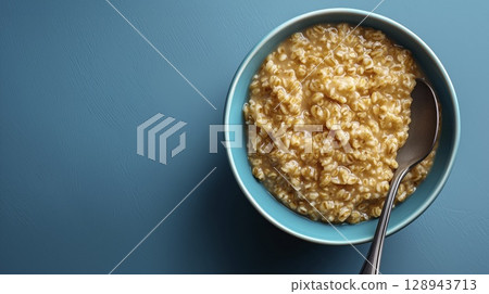 Cooked barley oat porridge in turquoise bowl, top view and blue background, copy space 128943713