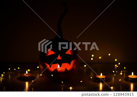 A carved Halloween pumpkin. Jack-o'-lantern glowing with a candle inside on a surface with lighting. Halloween festive spooky atmosphere concept 128943915