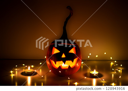 A carved Halloween pumpkin. Jack-o'-lantern glowing with a candle inside on a surface with lighting. Halloween festive spooky atmosphere concept A carved Halloween pumpkin. Jack-o'-lantern glowing with a candle inside on a surface with lighting. Halloween festive spooky atmosphere concept 128943916