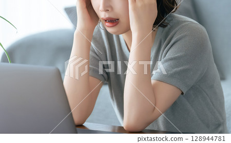 A woman holding her head while using a computer A woman holding her head while using a computer 128944781