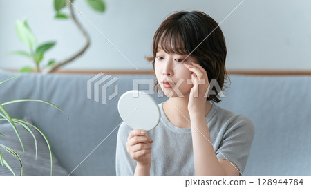 A woman checking her eyes in the mirror 128944784