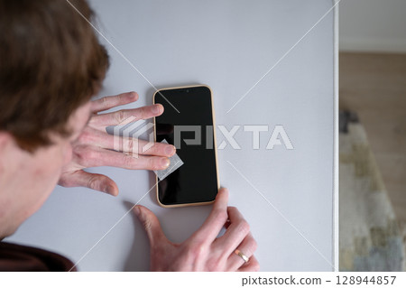 Man cleaning smartphone screen with dry wipe before applying screen protector Man cleaning smartphone screen with dry wipe before applying screen protector 128944857