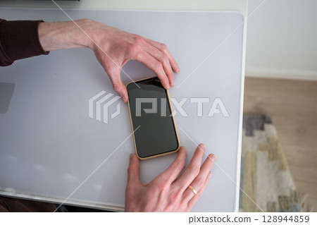 Man applying screen protector to smartphone on white desk 128944859